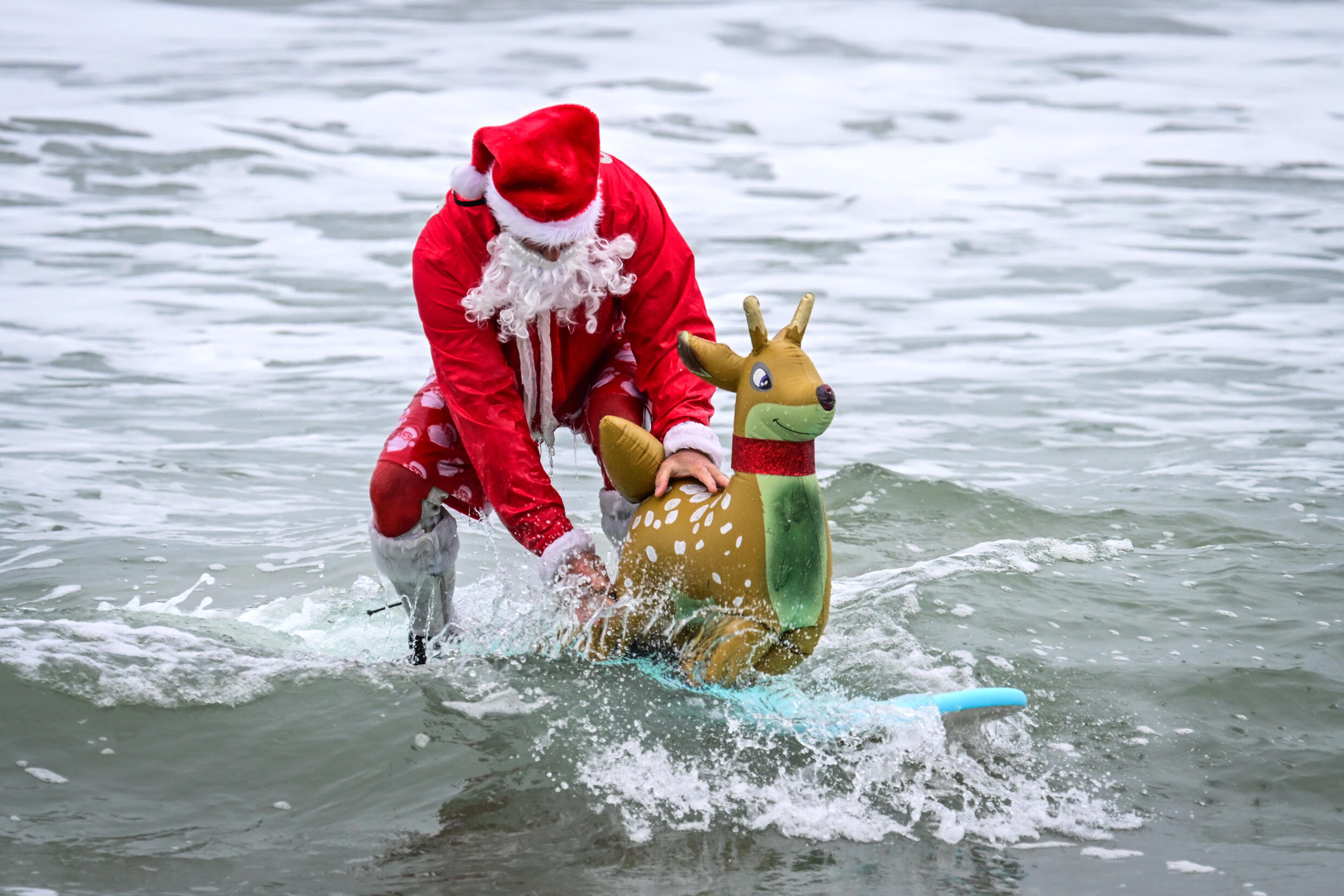 A surfer dressed as Santa Claus participates in the 16th annual 'Surfing Santas' event on Christmas Eve 2024 in Cocoa Beach, Florida